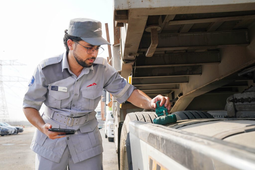 RTA and Dubai Police officers inspecting heavy vehicle tyres and distributing multi-lingual safety manuals to truck drivers at a highway rest area.