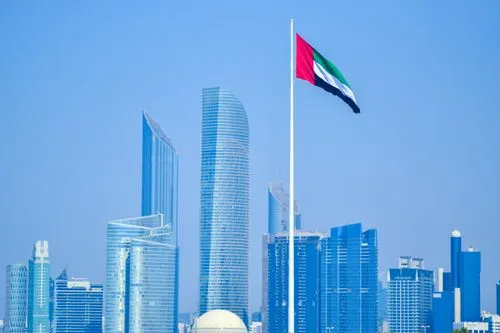 UAE flag waving in Abu Dhabi skyline under a clear sky.